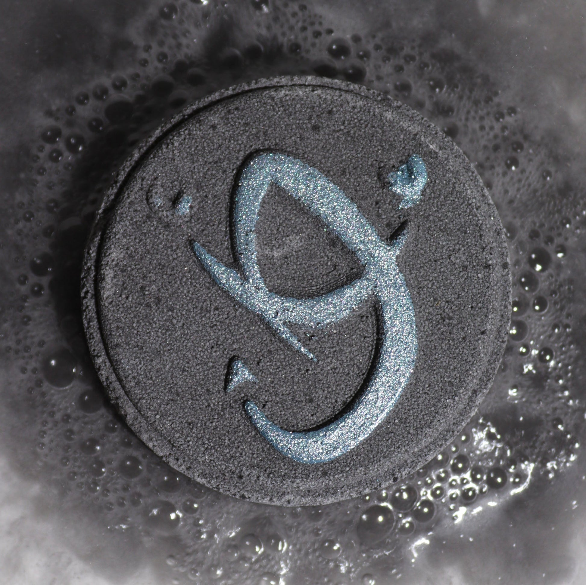 Scorpio Zodiac Bath Bomb Fizzers - Obsidian & Dark Coffee - 2 Pack, close-up of a dark grey fizzer embossed with the Scorpio symbol by Quintessential Holistic Health Ltd