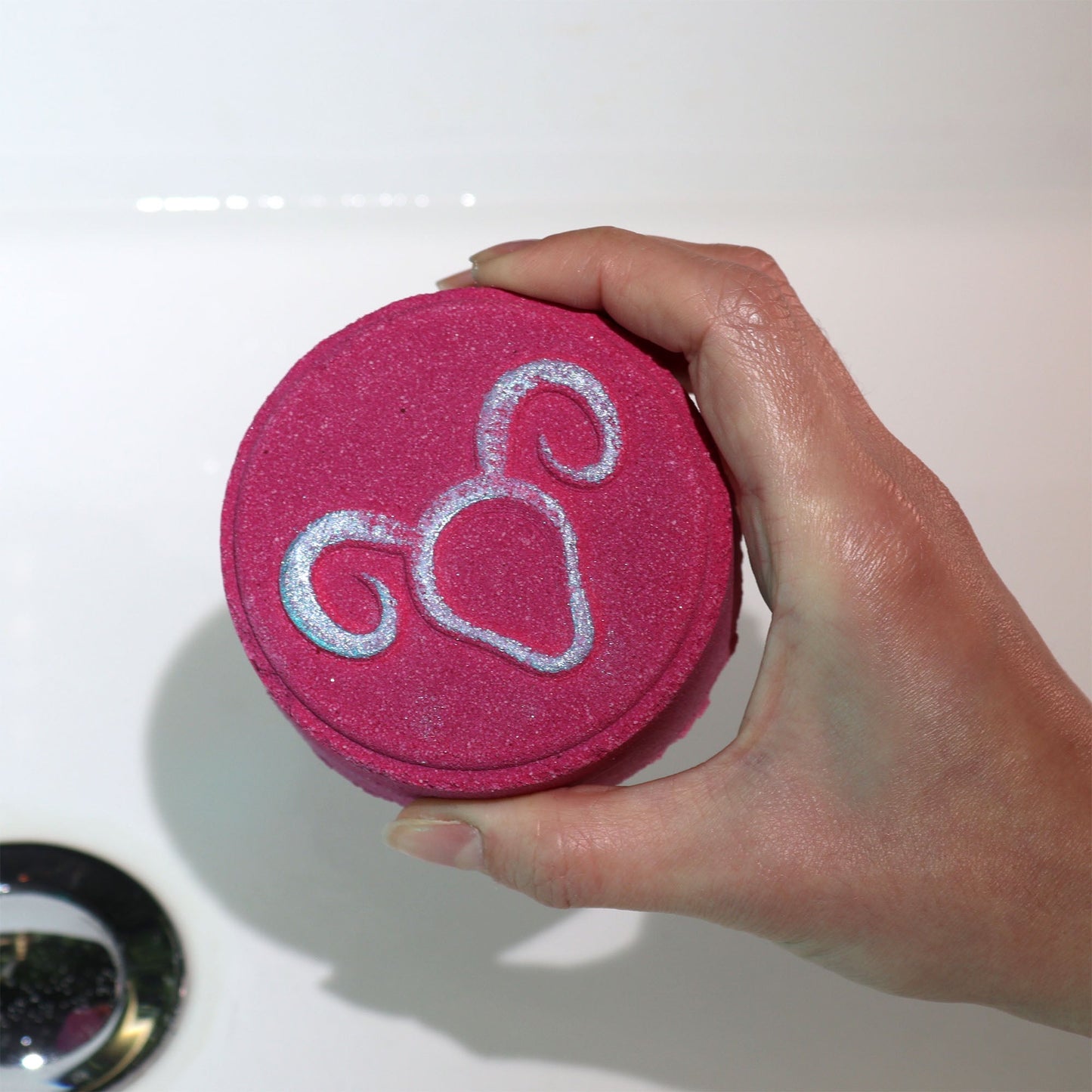 Sagittarius Bath Bomb Fizzers - Turquoise Dewness - 2 Pack, deep pink round fizzer embossed with the Sagittarius symbol and held in one hand by Quintessential Holistic Health Ltd