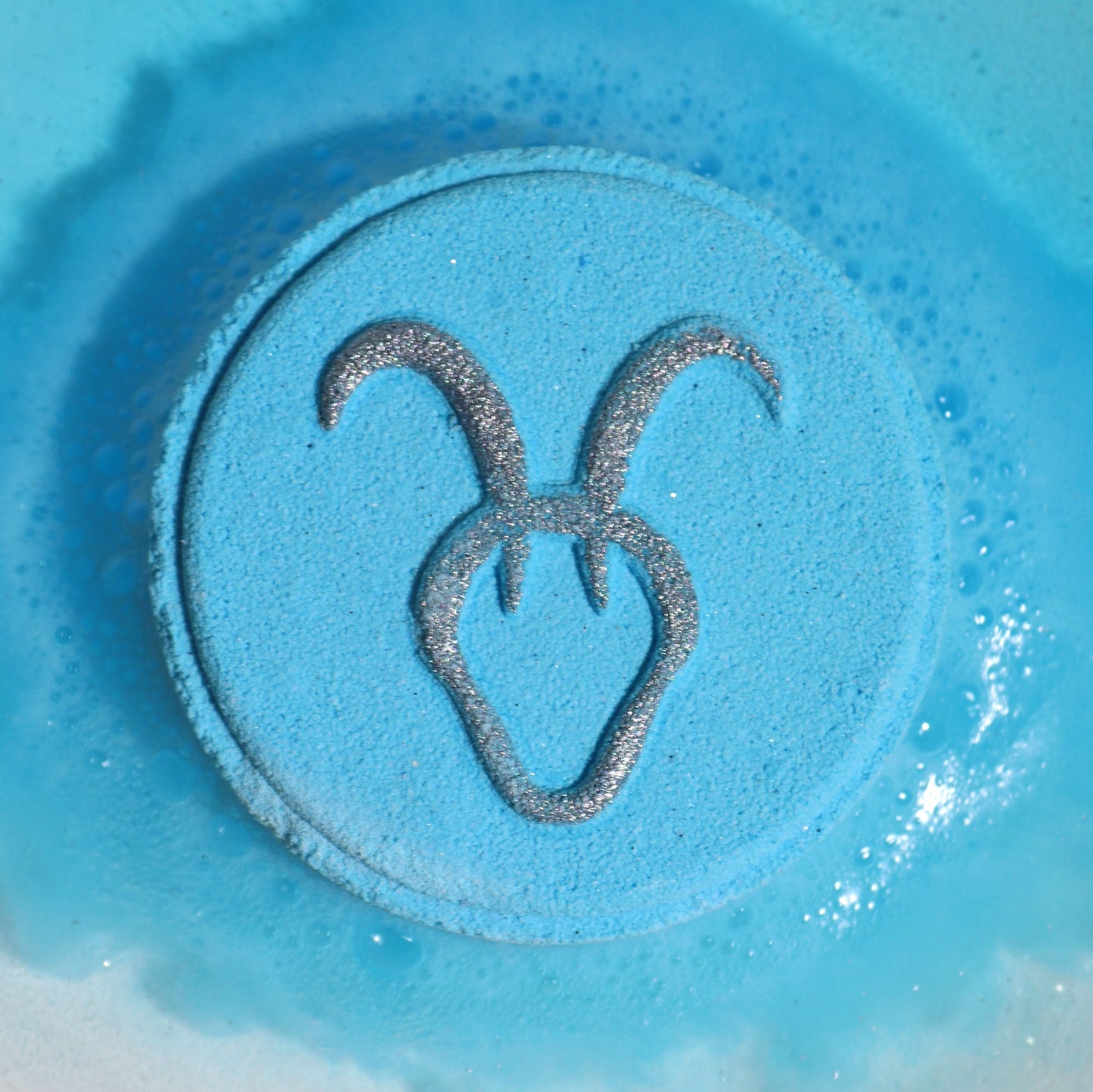 Capricorn Bath Bomb Fizzers - Lapis Lazuli - 2 Pack, close-up of a blue round fizzer embossed with the Capricorn symbol by Quintessential Holistic Health Ltd
